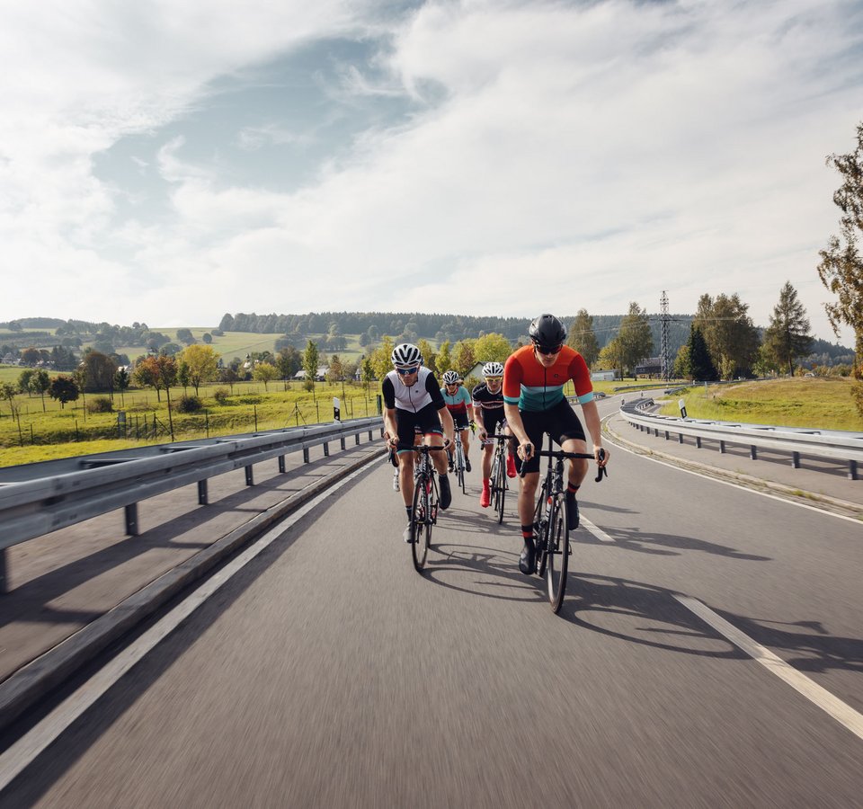 7 Reasons to Roadbike @Erzgebirge © Felix Meyer Vier Radfahrer fahren auf einer Landstraße durch eine grüne Landschaft.