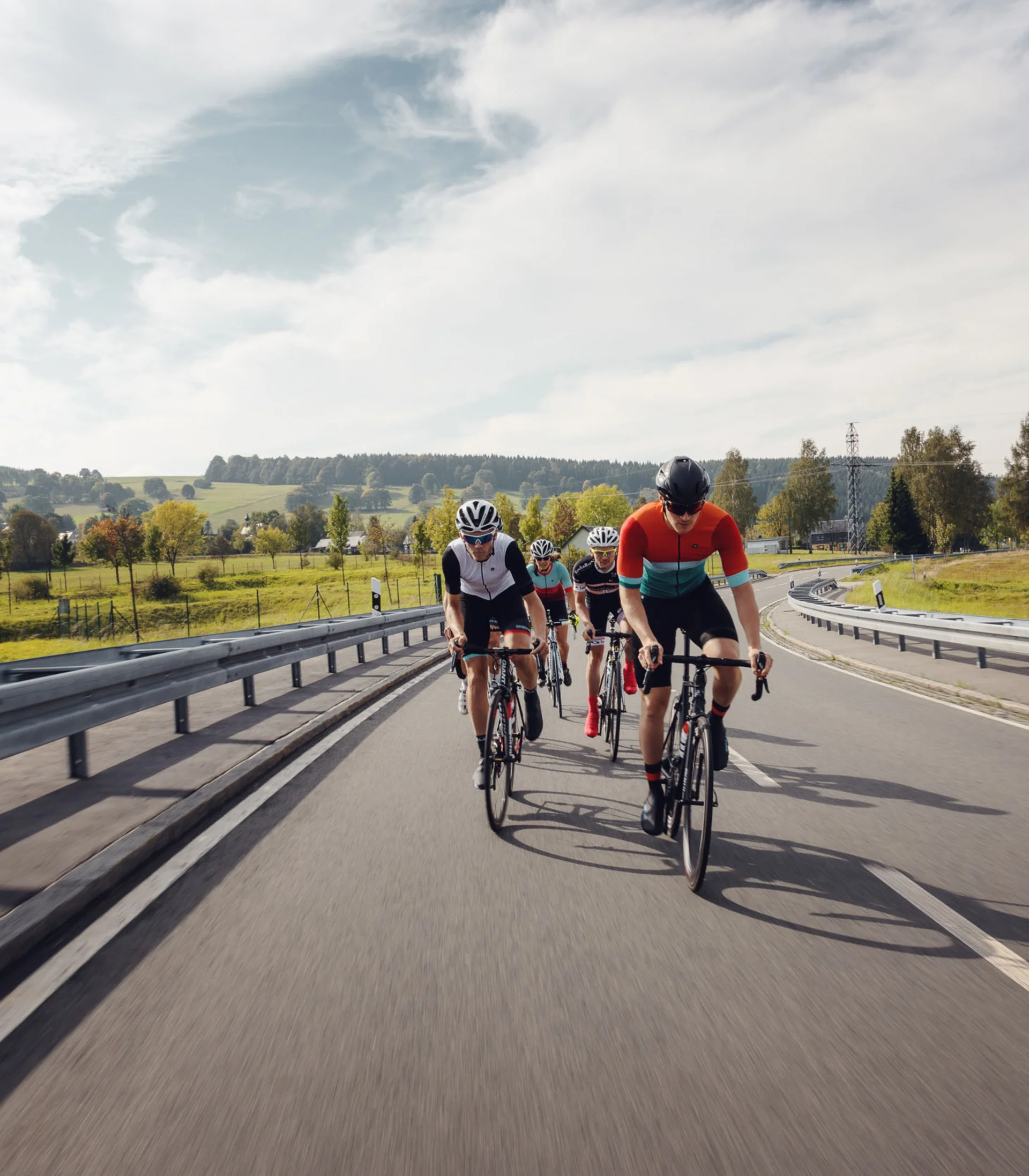 Quattro ciclisti pedalano su una strada di campagna in un paesaggio verde.