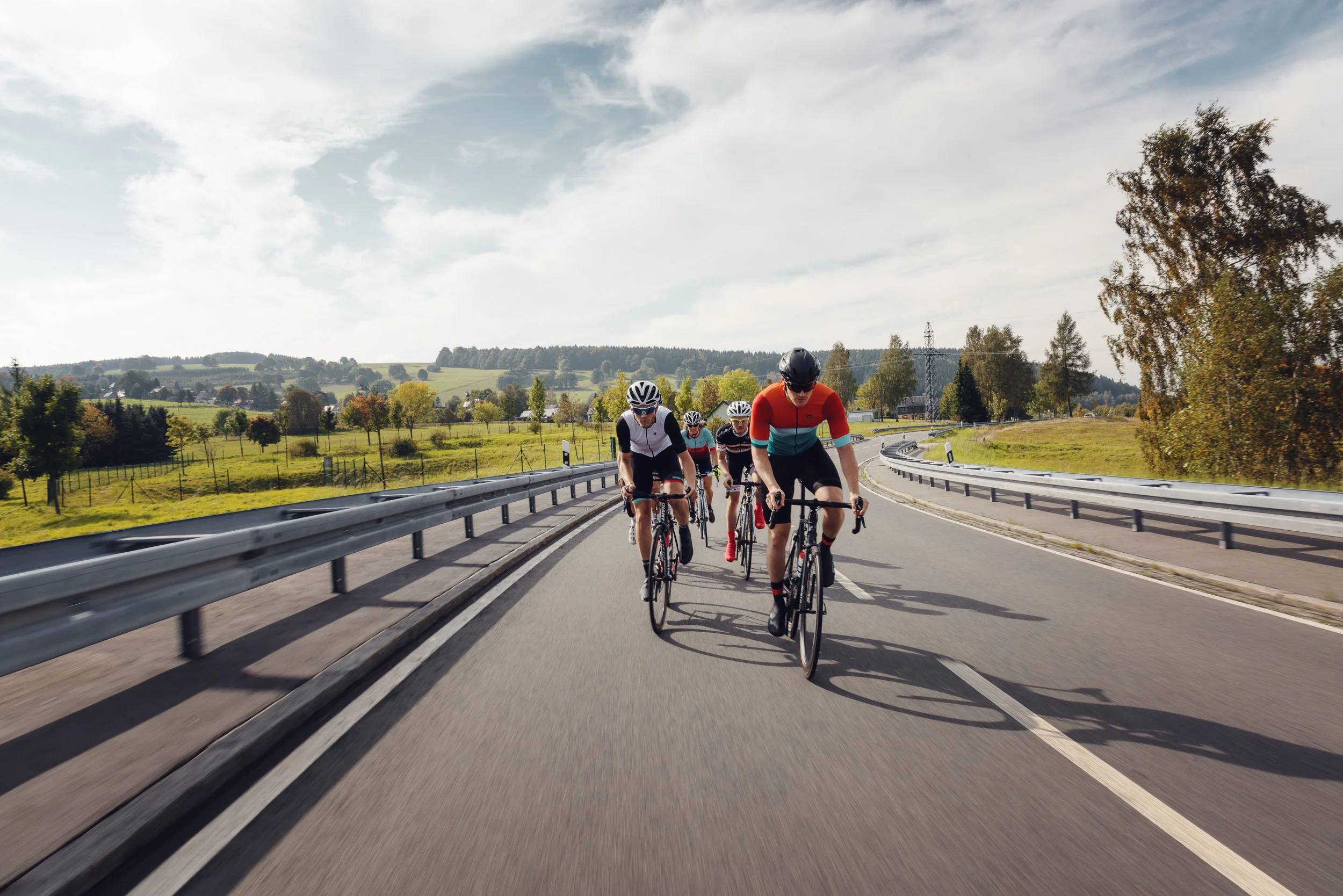 Four cyclists riding on a country road through green countryside.