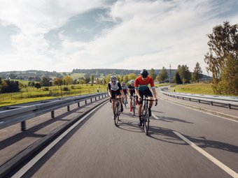 Vier Radfahrer fahren auf einer Landstraße durch eine grüne Landschaft.