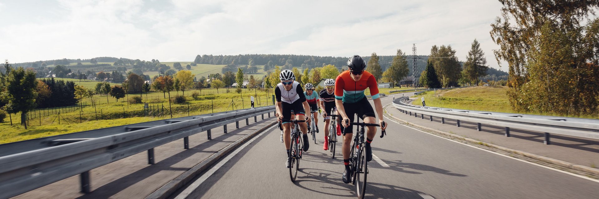 Quattro ciclisti pedalano su una strada di campagna in un paesaggio verde.