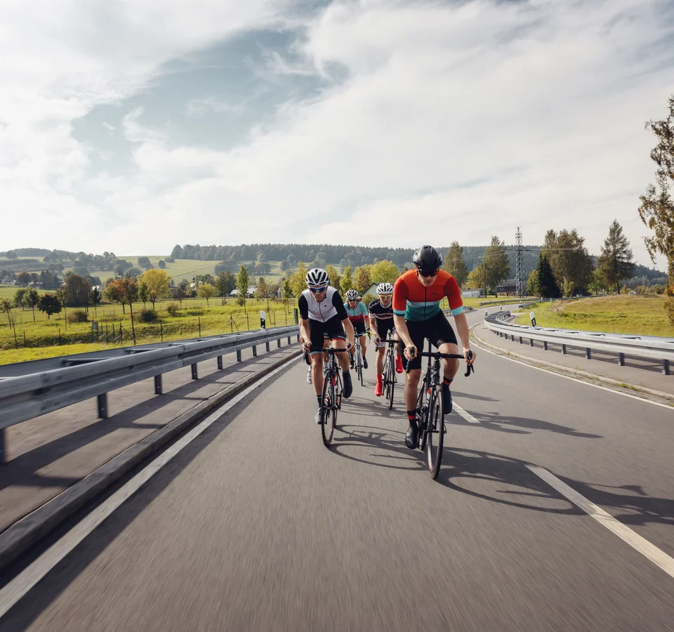 7 Reasons to Roadbike @Erzgebirge © Felix Meyer Vier Radfahrer fahren auf einer Landstraße durch eine grüne Landschaft.