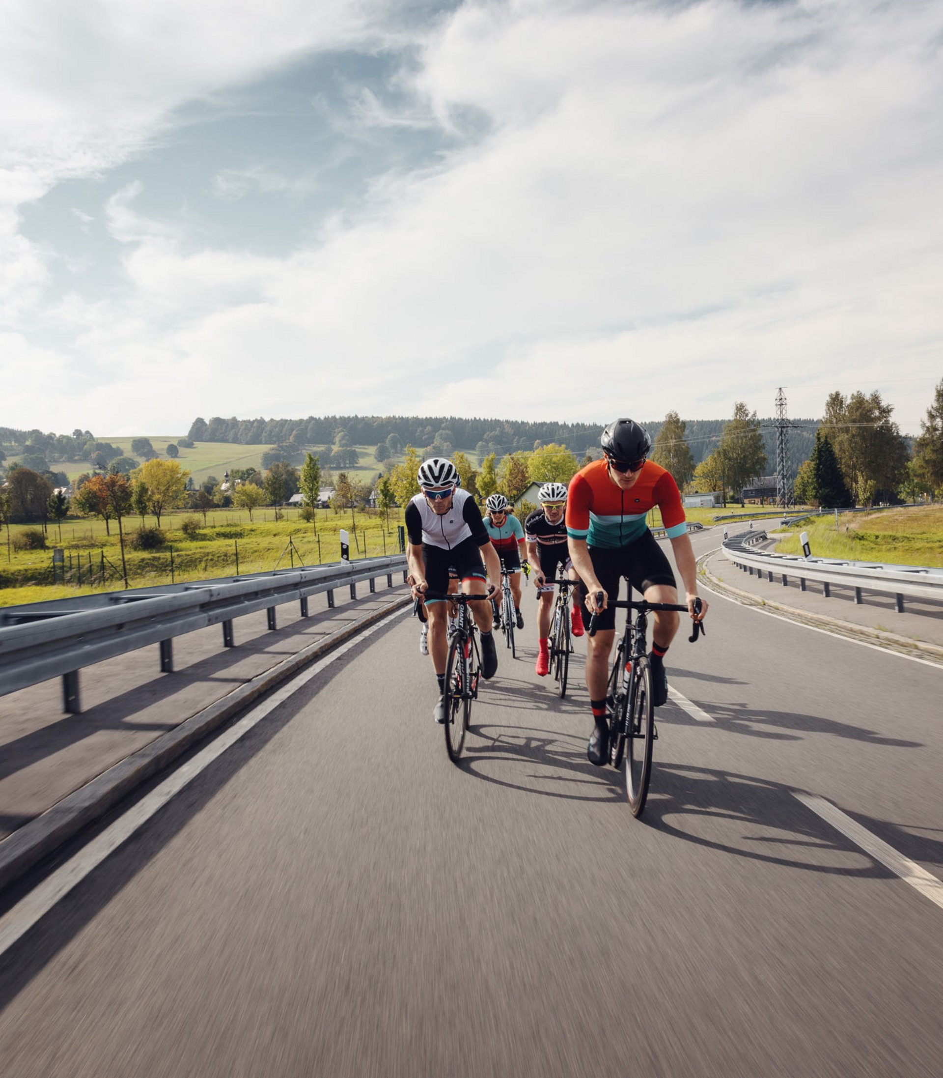 Vier Radfahrer fahren auf einer Landstraße durch eine grüne Landschaft.