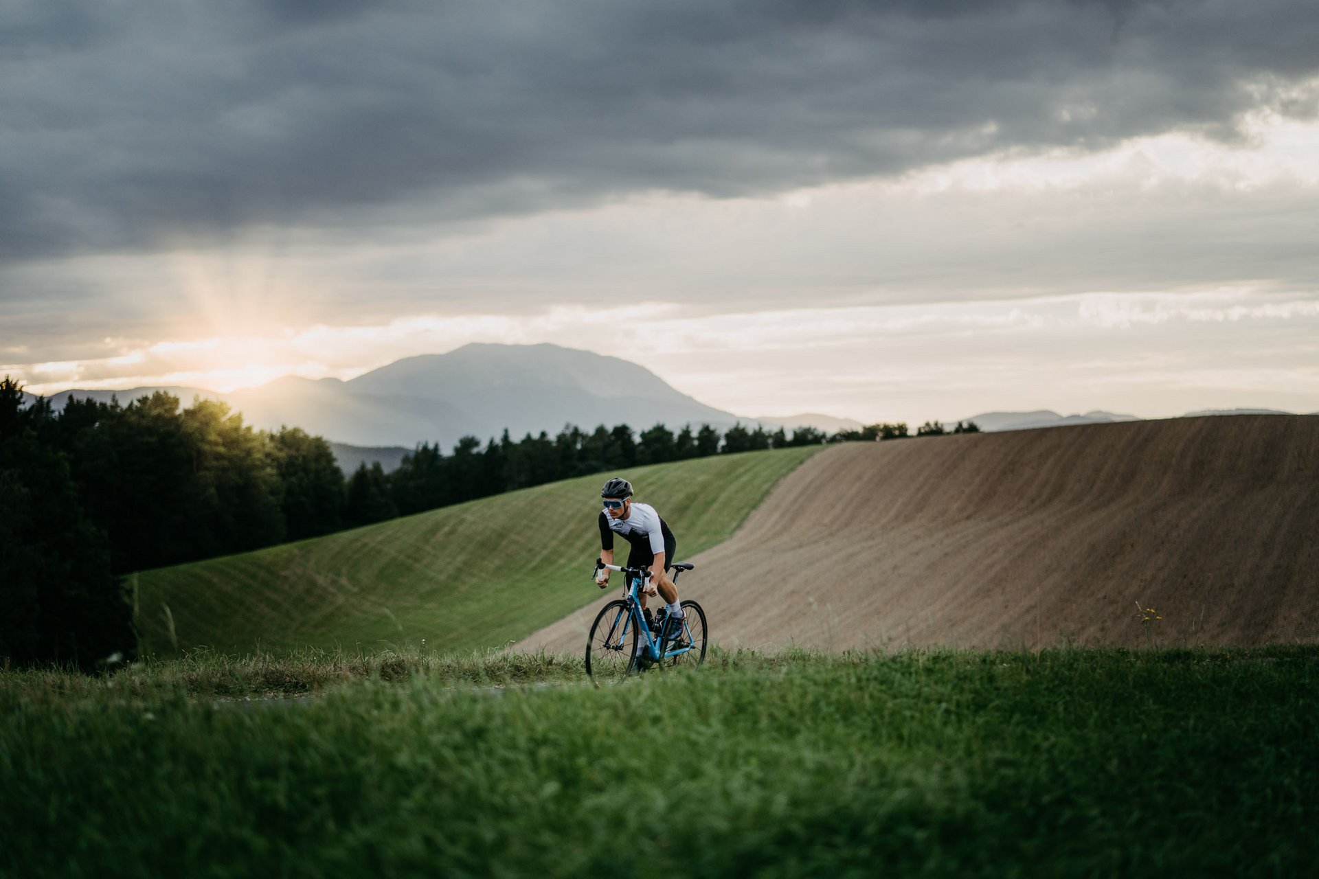 Fietser rijdt door heuvelachtig landschap bij zonsondergang