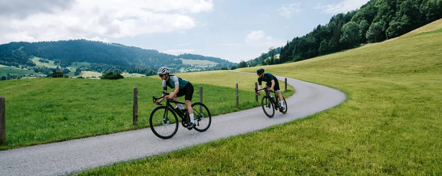 A racing bike weekend in the Bregenzerwald © Bregenzerwald Tourismus - Christina Neubauer Two cyclists riding on a winding country road through green hills.