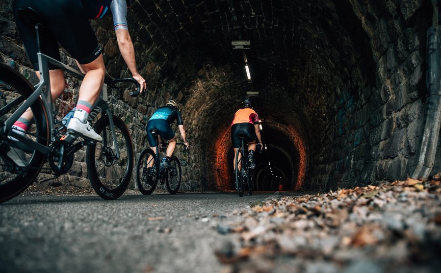 Drie fietsers rijden door een verlichte stenen tunnel