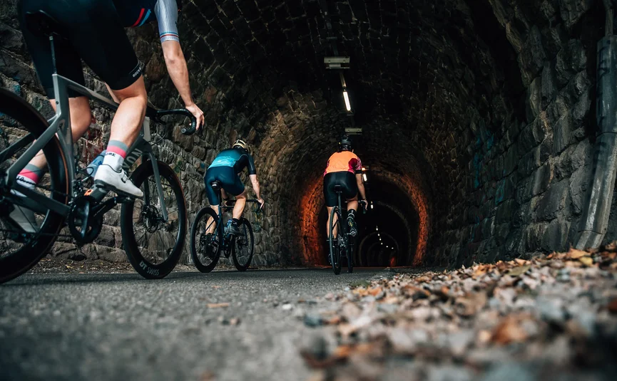 Drei Radfahrer fahren durch einen beleuchteten Steintunnel