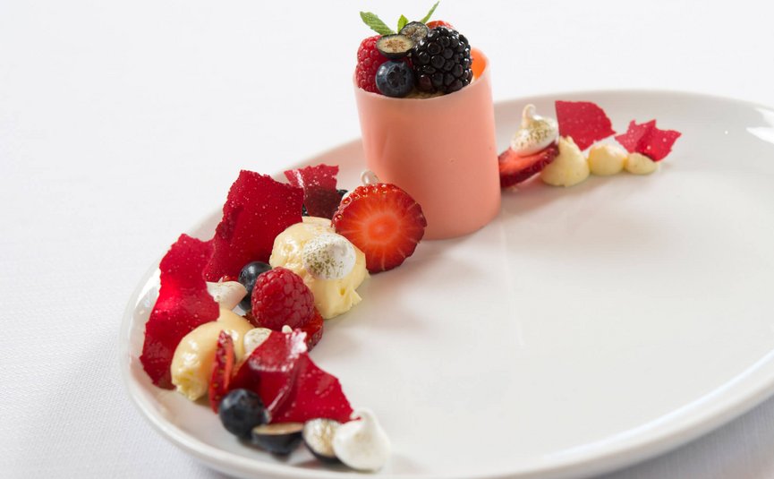 Gourmet-Dessert mit Beeren, roten Fruchtcoulis und Creme auf weißem Teller