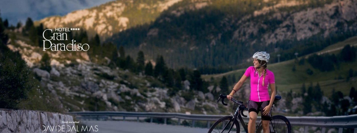 Frau mit Fahrrad auf Bergstraße vor Berglandschaft bei Hotel Gran Paradiso