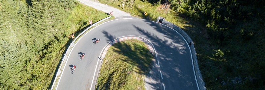 Three cyclists riding on a hairpin road in a forested area