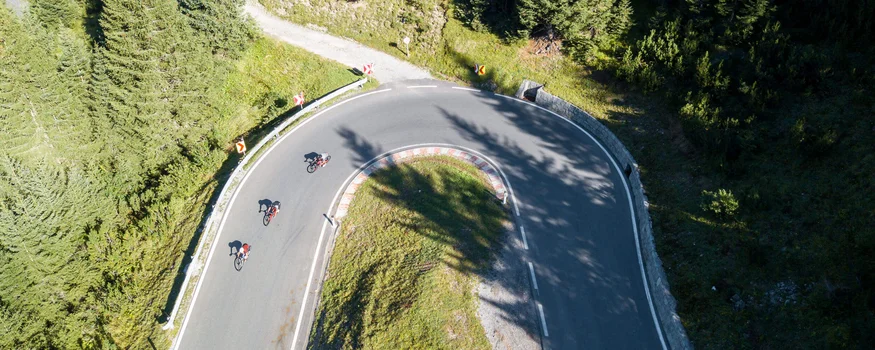 Drei Radfahrer fahren auf einer Serpentinenstraße in einem bewaldeten Gebiet