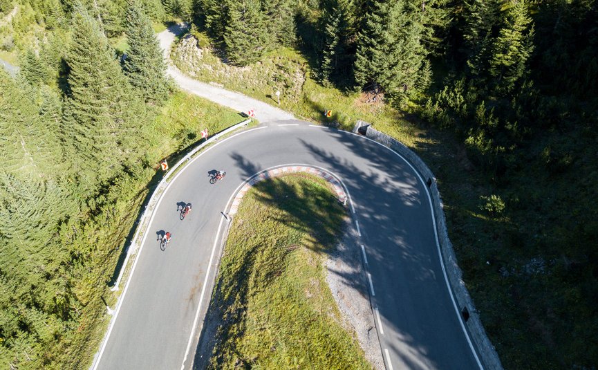 Three cyclists riding on a hairpin road in a forested area