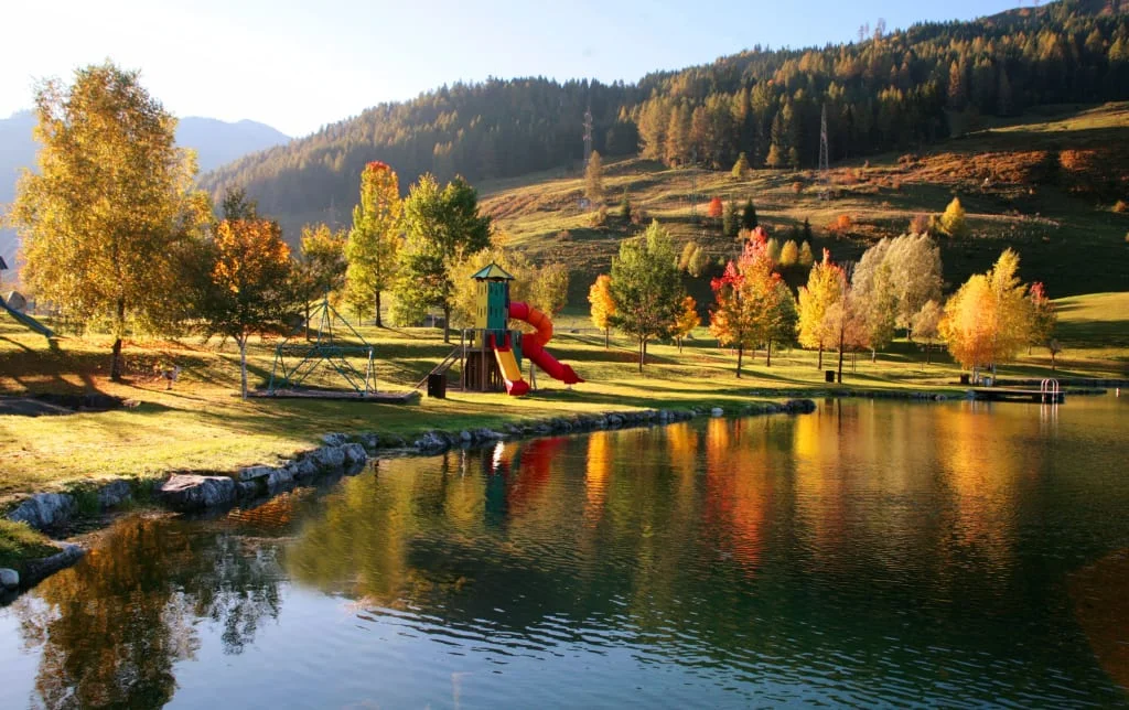 Spielplatz am See vor herbstlich gefärbten Bäumen und bewaldeten Bergen