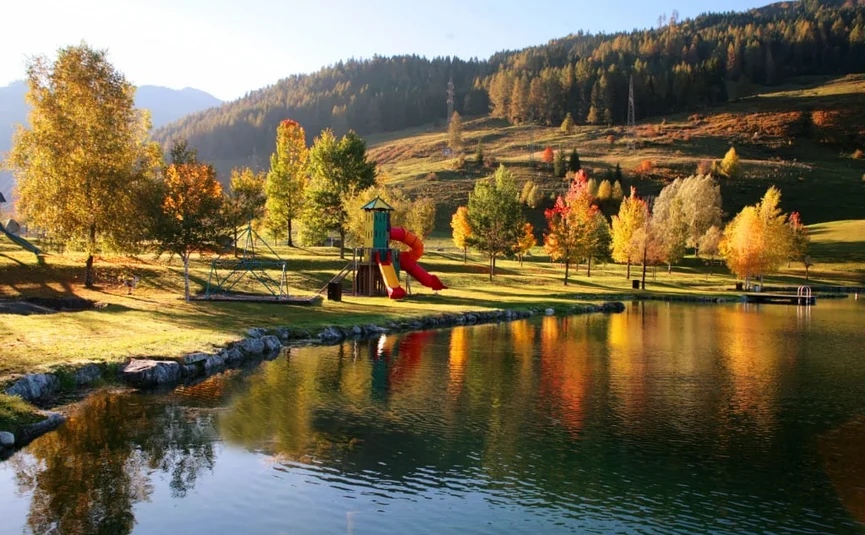 Goldener Herbst – 7 Nächte Wohlfühl-Camping für ZWEI Spielplatz am See vor herbstlich gefärbten Bäumen und bewaldeten Bergen