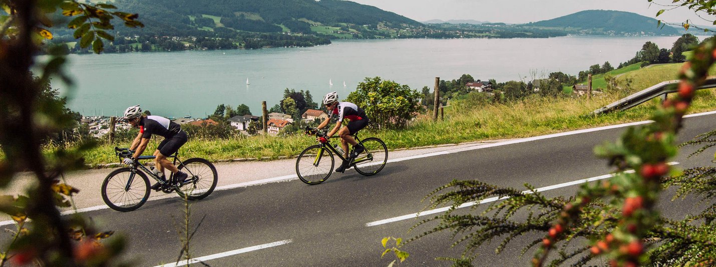 Two cyclists on country road with mountain and lake view