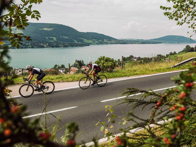 Ein Rennrad-Wochenende im SalzburgerLand – Salzkammergut © SalzburgerLand - Stefan Schopf for WOM Medien Zwei Radfahrer auf Landstraße mit Berg- und Seeblick