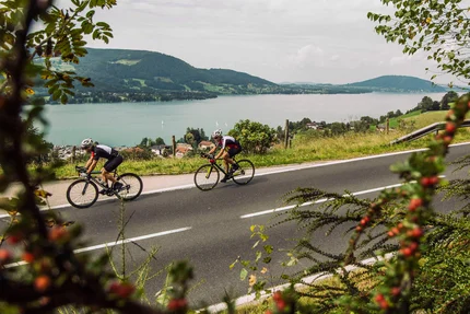 Due ciclisti su strada di campagna con vista su montagne e lago