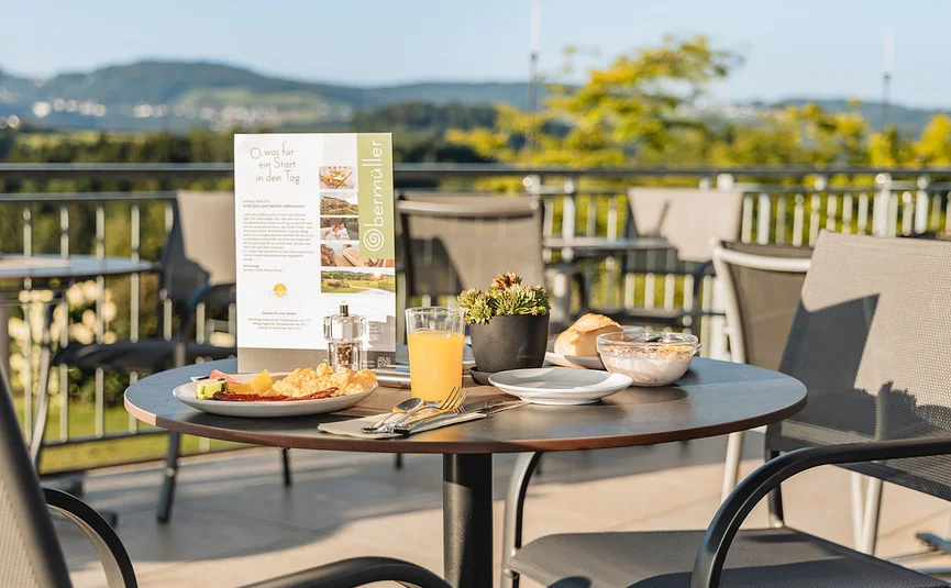 Frühstückstisch mit Eiern, Orangensaft und Brötchen auf Terrasse mit Aussicht