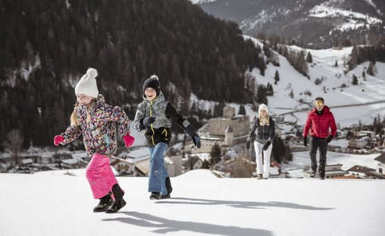 Twee kinderen en twee volwassenen lopen in de sneeuw met bergen en dorp op achtergrond