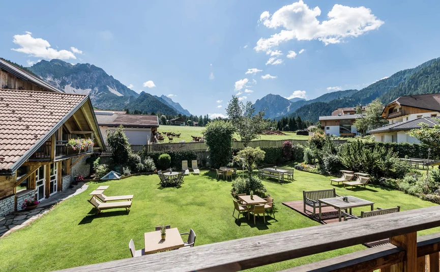 Garten mit Tischen und Liegestühlen vor Bergen unter klarem Himmel
