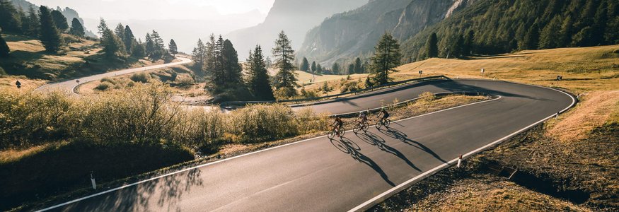 Three cyclists riding on a winding mountain road in sunlight