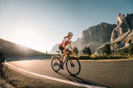Frau fährt Rennrad auf Bergstraße bei Sonnenaufgang