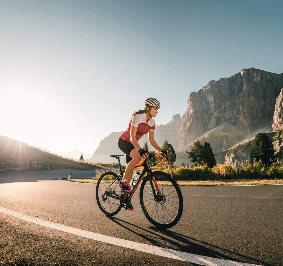 Woman cycling on mountain road at sunrise