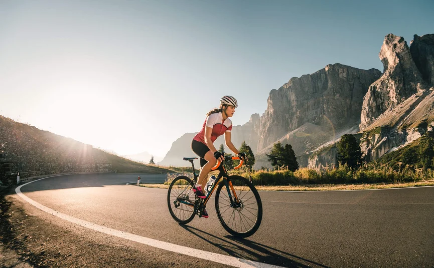 Vacanze in bici da corsa in Alta Badia © Molography Donna in bicicletta su strada di montagna all'alba