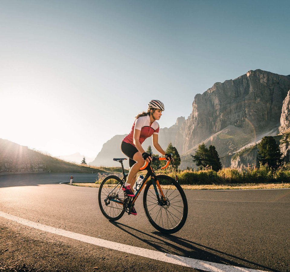 Frau fährt Rennrad auf Bergstraße bei Sonnenaufgang