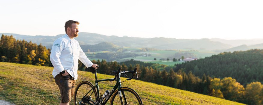 Uomo con bici da corsa su sentiero che guarda colline al tramonto