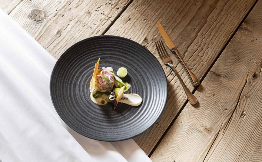 Artistically plated gourmet dish on black plate with cutlery on wooden table