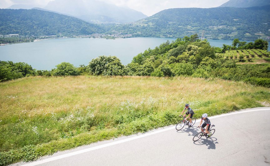 Due ciclisti su una strada di montagna con vista su un lago e montagne