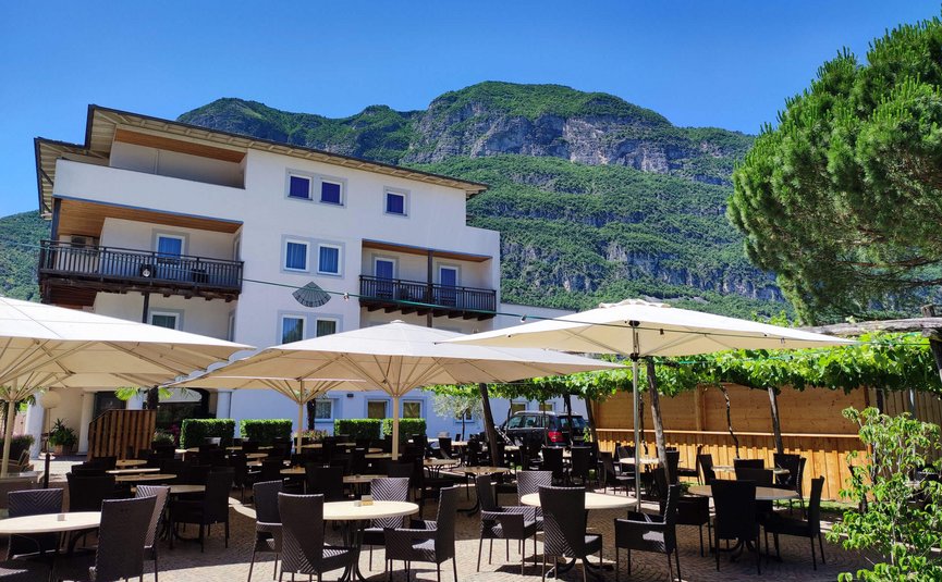 Sonnenterrasse mit Tischen und Stühlen vor einem Hotel mit Bergkulisse