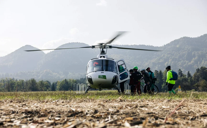 Gruppe von Radfahrern besteigt Hubschrauber auf einem Feld mit Bergen im Hintergrund
