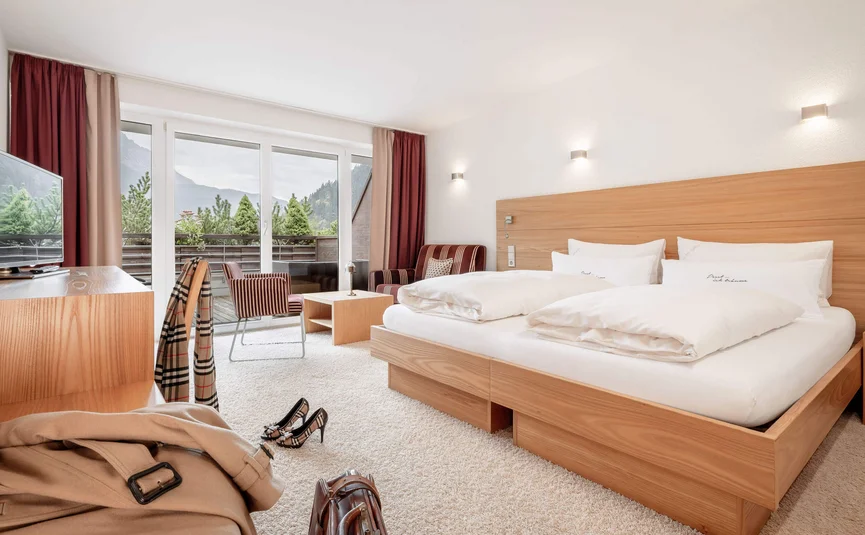 Helles Hotelzimmer mit großem Bett und Balkonblick auf Berge