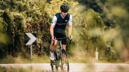 Radfahrer fährt auf Landstraße vor einer Burg auf einem Hügel