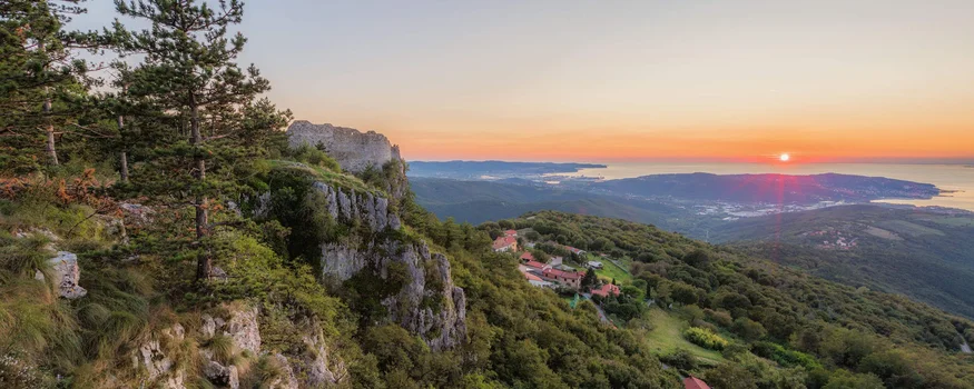 Sonnenuntergang über bewaldeten Hügeln mit Blick auf Meer und Felsenklippen