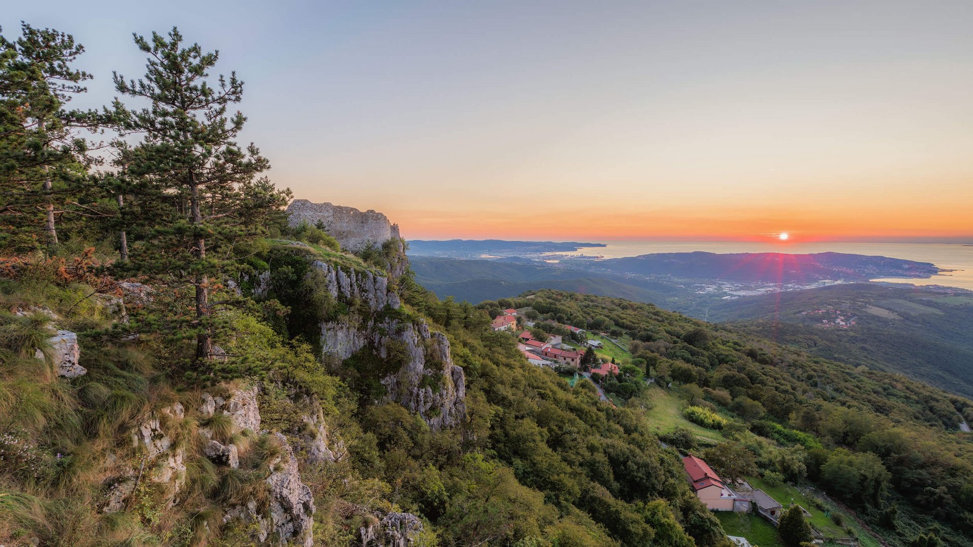 Sonnenuntergang über bewaldeten Hügeln mit Blick auf Meer und Felsenklippen