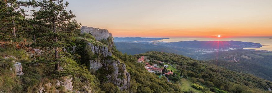 Sunset view over forested hills, cliffs, and distant sea coastline