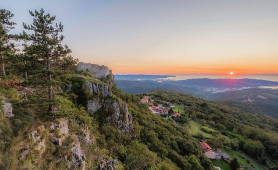 Tramonto su colline boschive con scogliere e vista sul mare