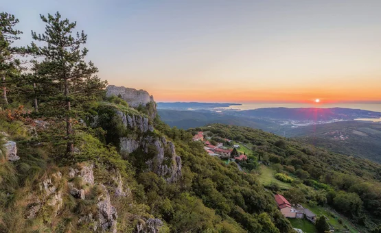 Sonnenuntergang über bewaldeten Hügeln mit Blick auf Meer und Felsenklippen