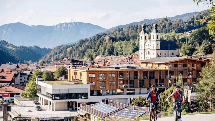 Zwei Menschen fahren Mountainbike vor Alpenstadt mit Kirche und Bergen