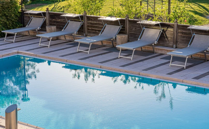 Cristallo Sport & Wellness Hotel **** © Andrea Acler Leere Sonnenliegen neben einem sauberen blauen Swimmingpool im Garten