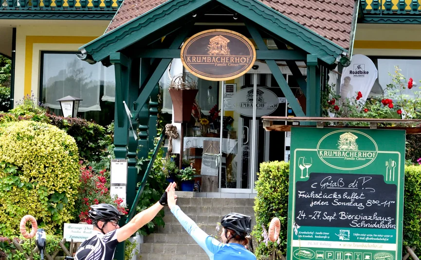 Due ciclisti danno il cinque davanti a una casa gialla con un cartello all'ingresso