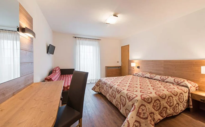 Bright hotel room with double bed, sofa, desk, and TV