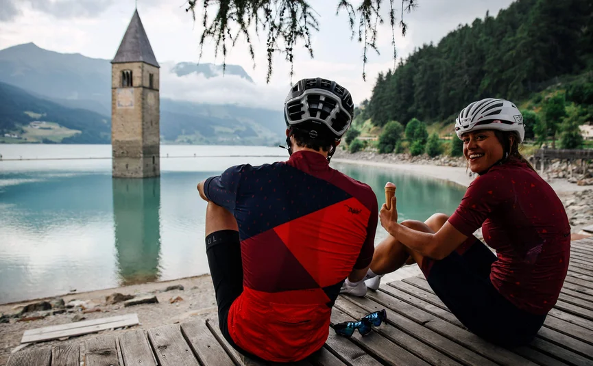 Two cyclists sitting by a lake with a submerged church tower