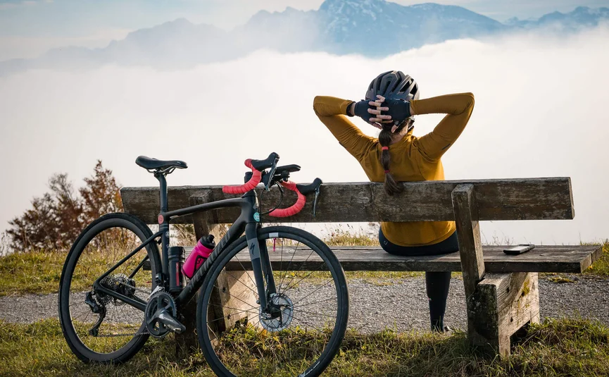 Radfahrerin sitzt auf Bank mit Blick auf Berge und Nebel