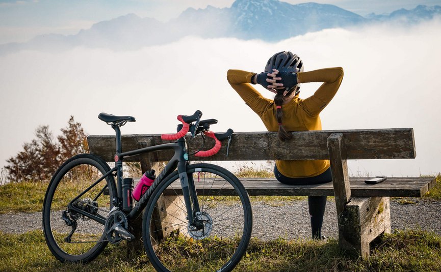 Ciclista seduta su panchina con vista su montagne e nebbia