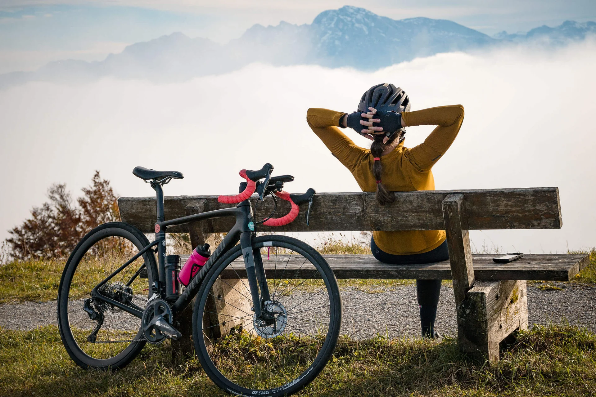 Roadbike Holidays © A Swiss with a pluse Radfahrerin sitzt auf Bank mit Blick auf Berge und Nebel