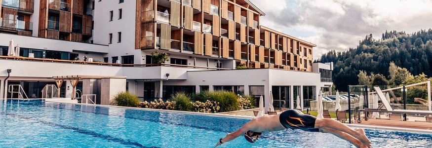 Mann taucht in einen Außenpool vor einem modernen Hotelgebäude ein